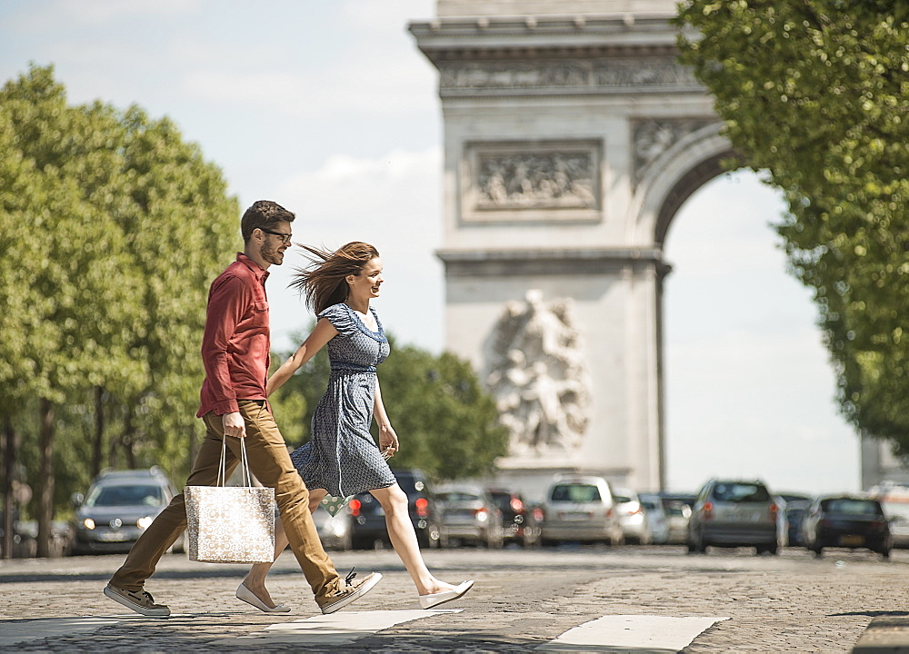 A couple hand in hand carrying shopping bags and crossing the road by a historic monument in the heart of a European city, France