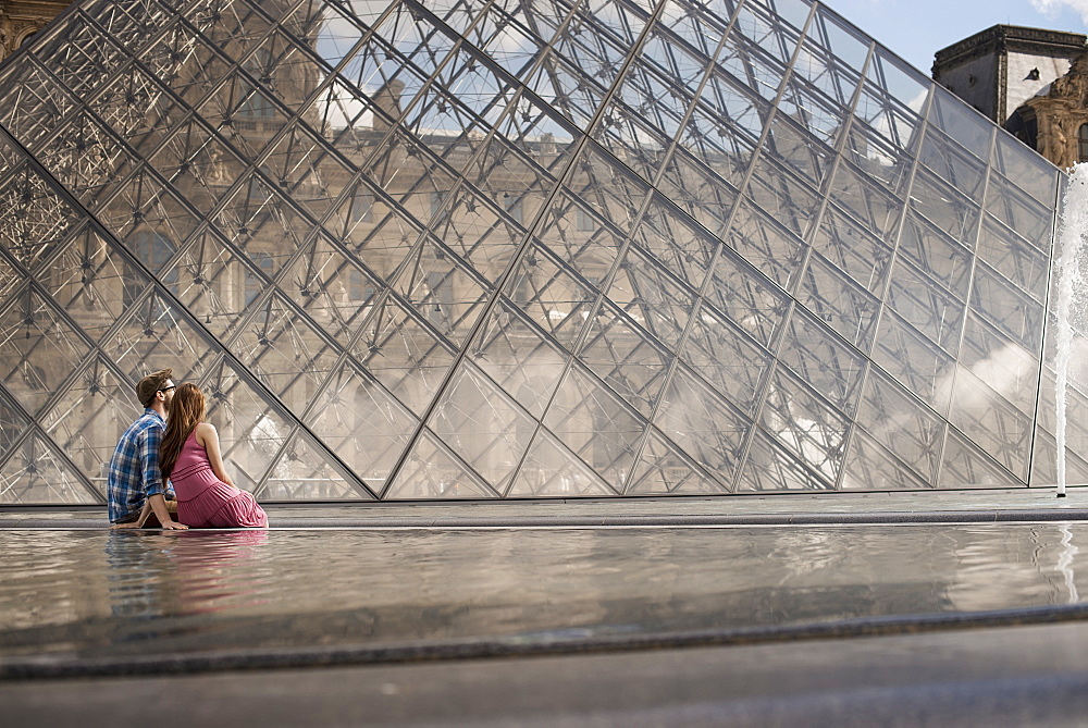 A couple in the courtyard of the Louvre museum, by the large glass pyramid. Fountains and water, France