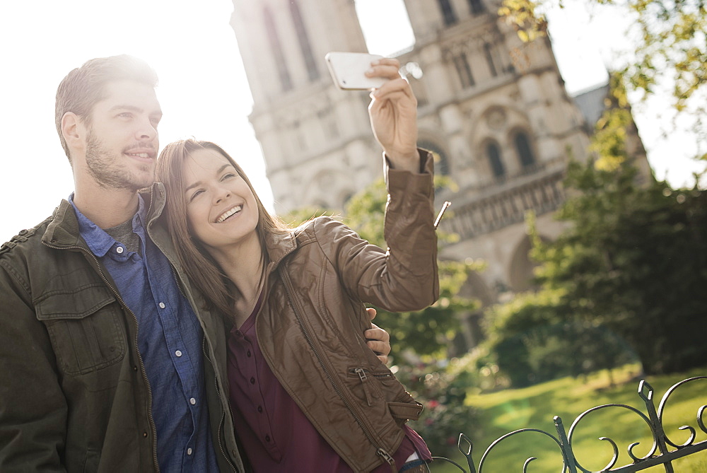 Two people, a couple standing close together taking a selfy outside the historic Notre Dame cathedral in Paris, France