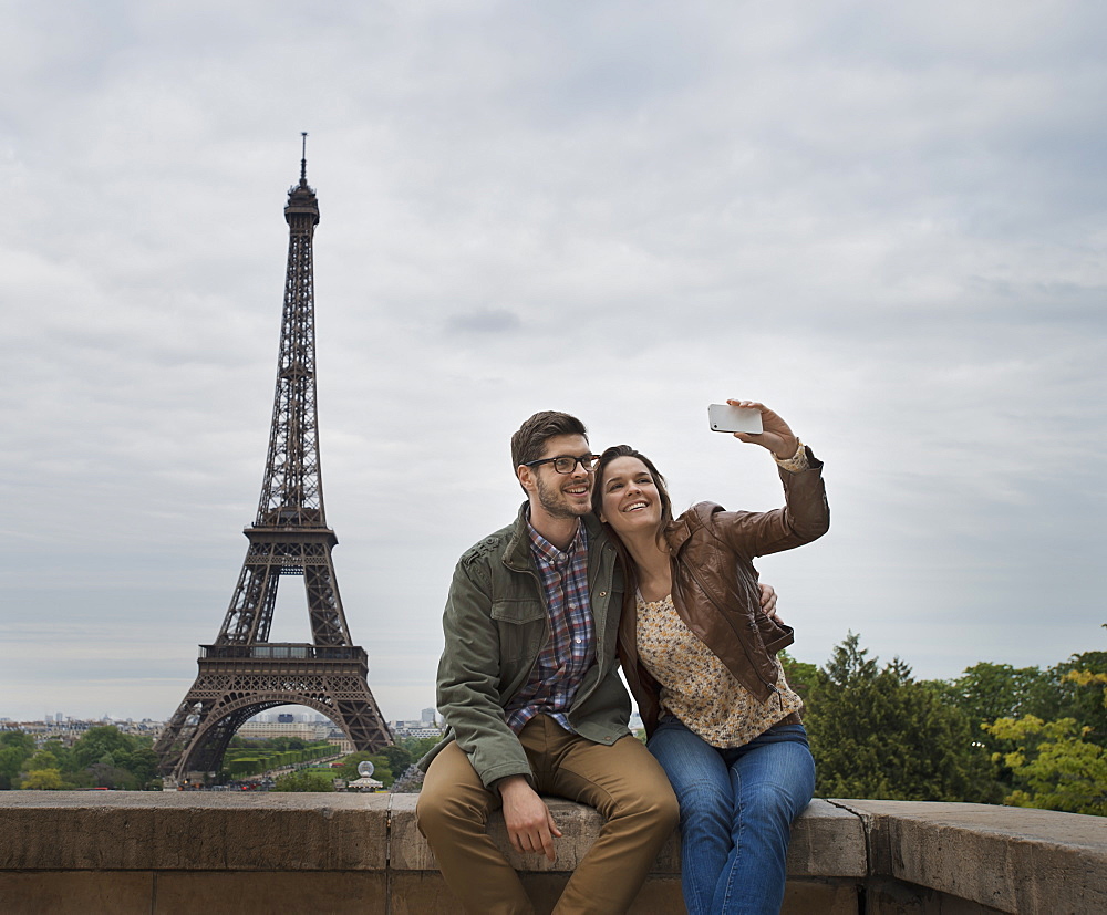 A couple seated side by side taking a selfy with the Eiffel Tower in the background, France