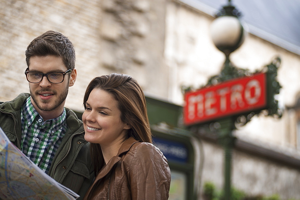 A couple consulting a map on a city street, under a classic Art Deco Metro sign, France