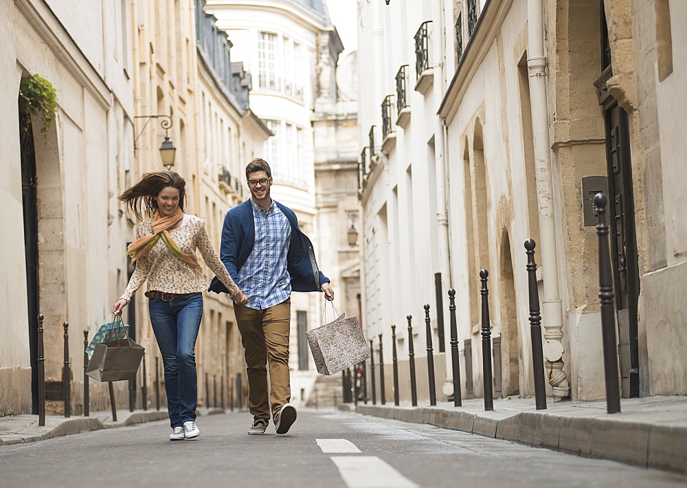 A couple walking along a narrow street in a historic city centre, with shopping bags, France