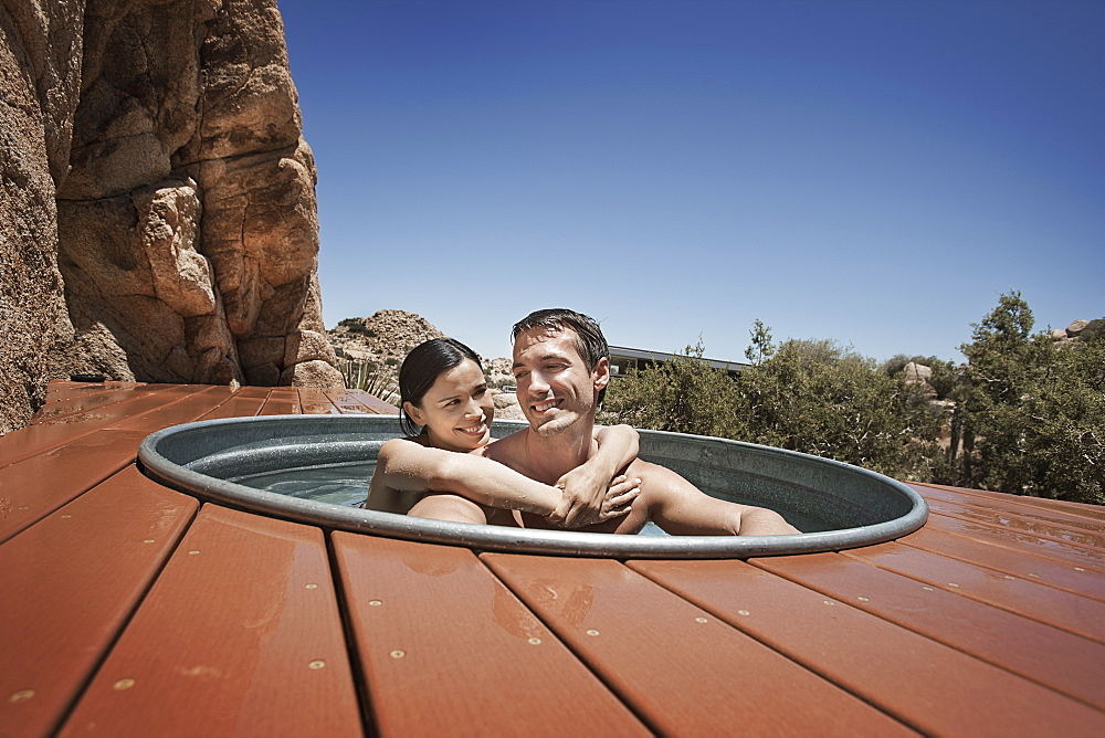 A man and woman on the terrace of an eco home, a low impact house in the desert landscape, in a sunken hot tub, United States of America