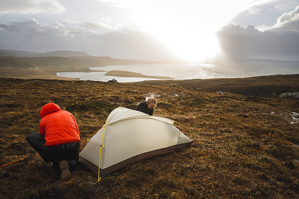 Two men holding and putting up a small tent in open space. Wild camping, Scotland, United Kingdom