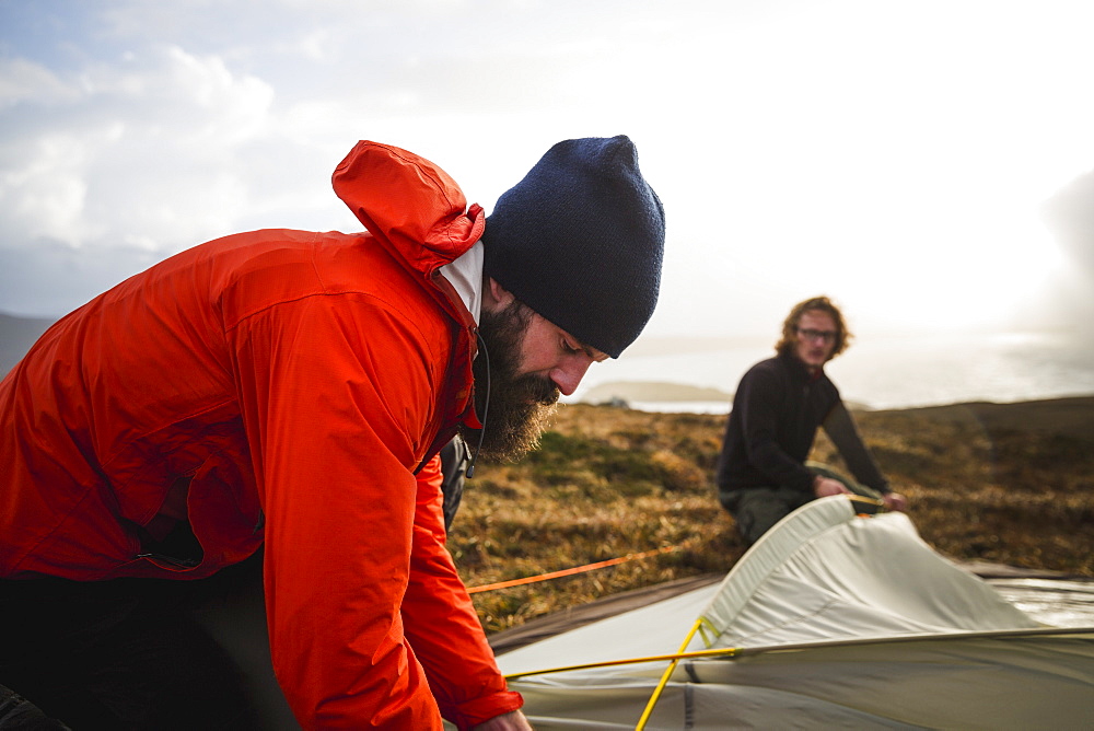 Two men holding and putting up a small tent in open space. Wild camping, Scotland, United Kingdom