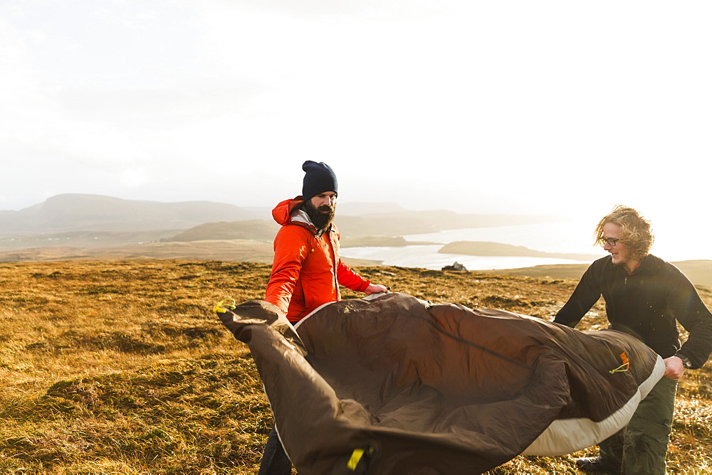 Two men holding and putting up a small tent in open space. Wild camping, Scotland, United Kingdom