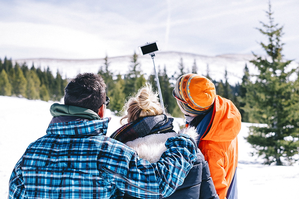 Three people, two men and a young woman in skiing gear posing for a selfie, one holding a selfie stick. 