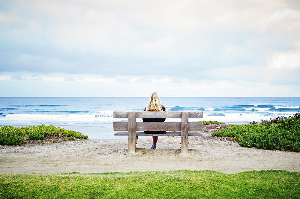 Rear view of a blond woman sitting on a beach by the ocean, United States of America