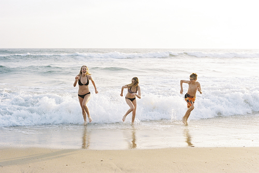 Three children playing on a sandy beach by the ocean.