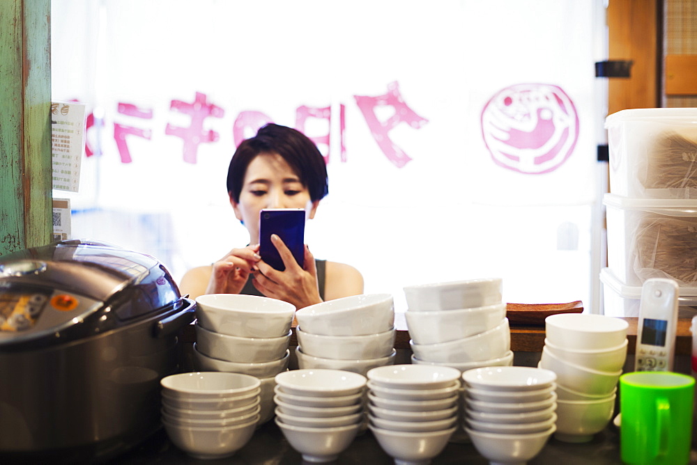 A woman using a smart phone at a noodle shop, Japan