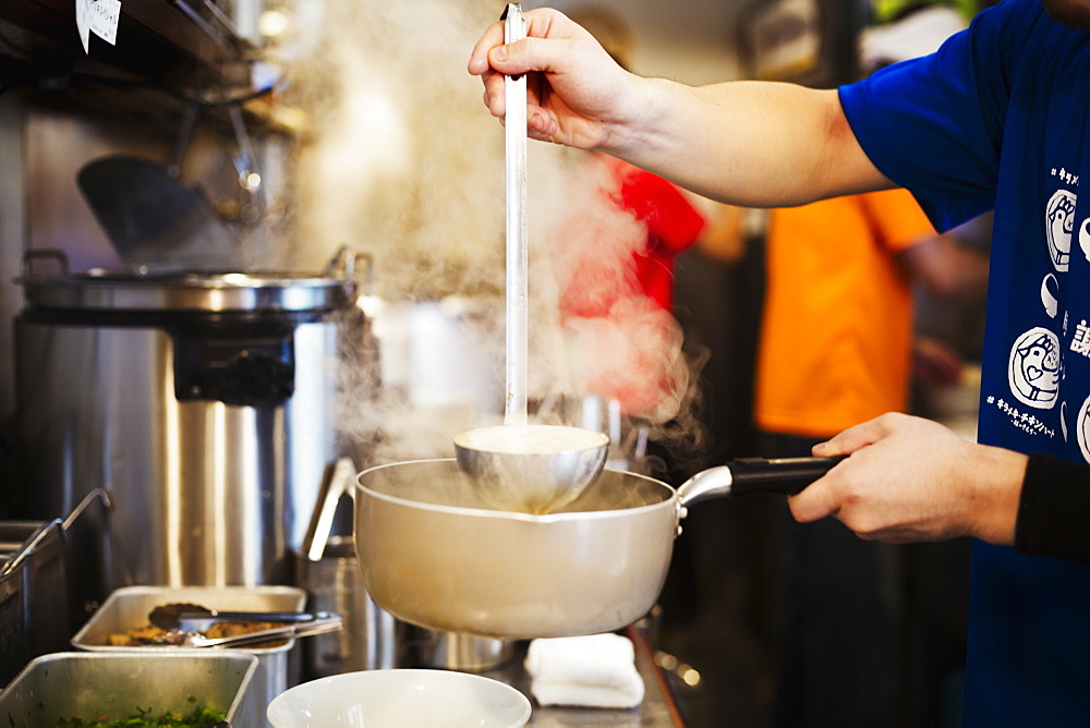 A ramen noodle shop kitchen. A chef preparing bowls of ramen noodles in broth, a speciality and fast food dish, Japan