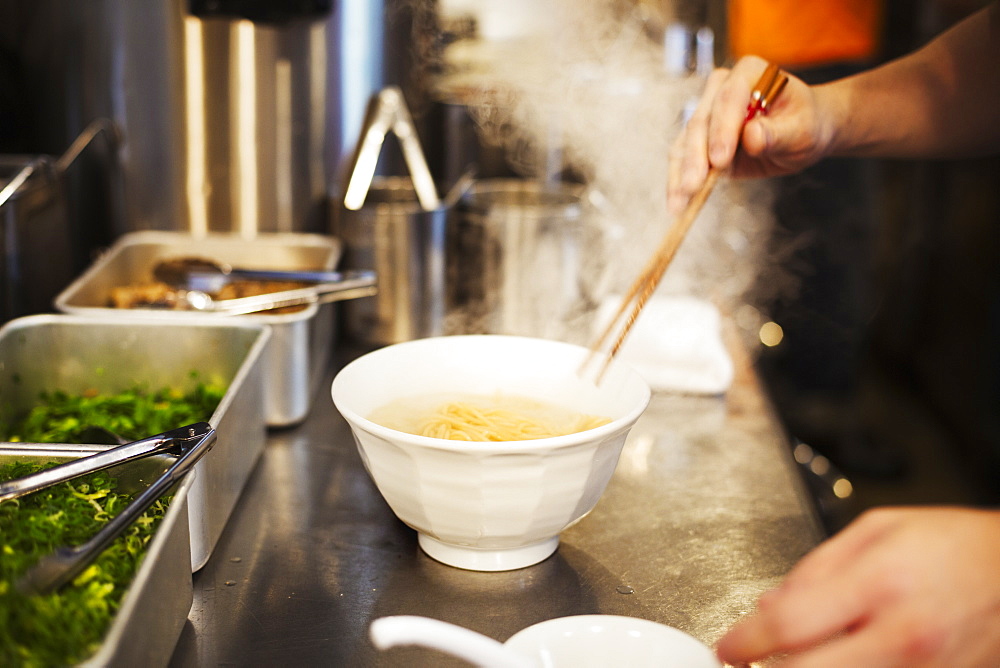 A ramen noodle shop kitchen. A chef preparing bowls of ramen noodles in broth, a speciality and fast food dish, Japan