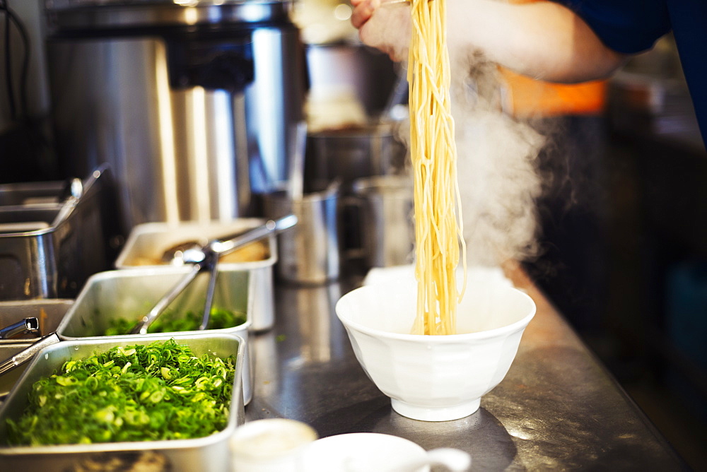 A ramen noodle shop kitchen. A chef preparing bowls of ramen noodles in broth, a speciality and fast food dish, Japan