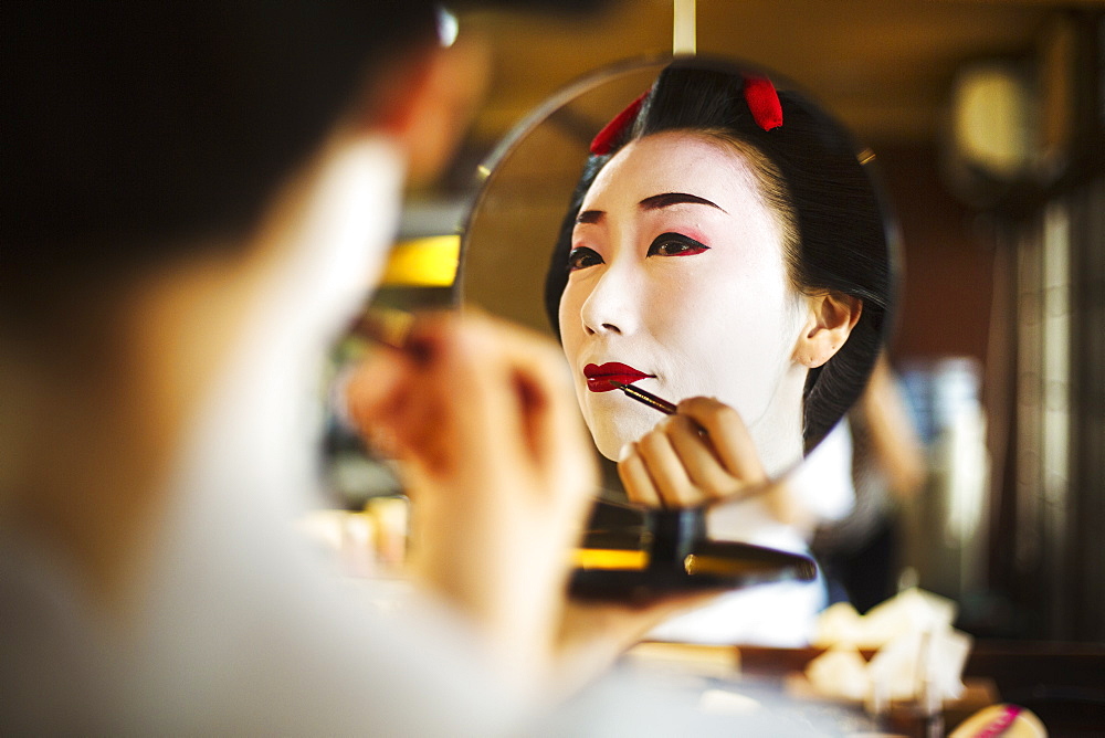 A modern geisha or maiko woman being prepared in traditional fashion, with white face makeup, Japan