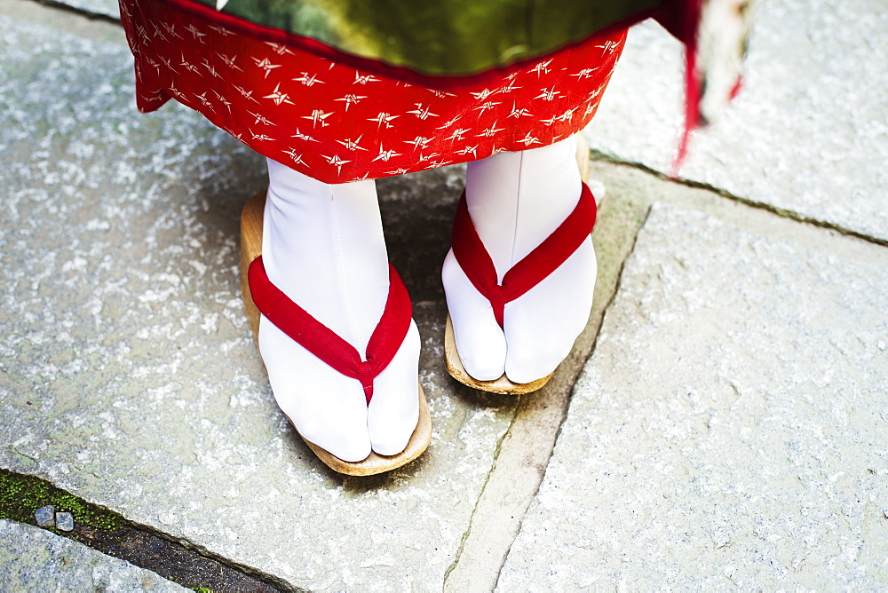 A traditional geisha woman's feet, in wooden soled sandals, with red straps and white stockings or tabi, Japan