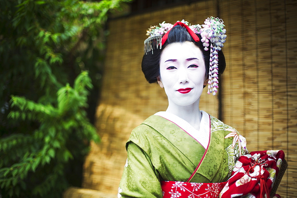 A woman dressed in the traditional geisha style, wearing a kimono and obi, with an elaborate hairstyle and floral hair clips, with white face makeup with bright red lips and dark eyes, Japan