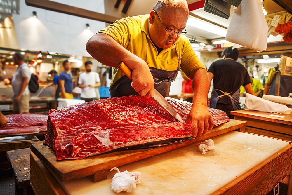 A traditional fresh fish market in Tokyo. A fishmonger working filleting a large fish on a slab. People in the background, Japan