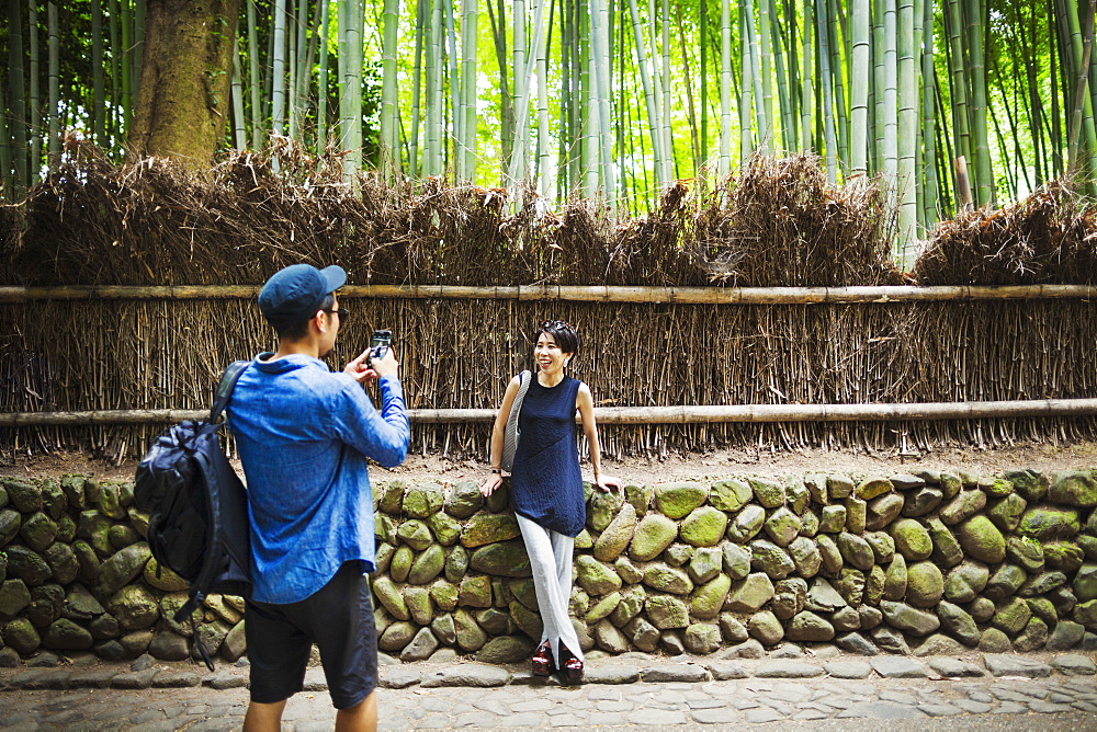 A man taking a photograph of a woman by a fence around woodland, Japan