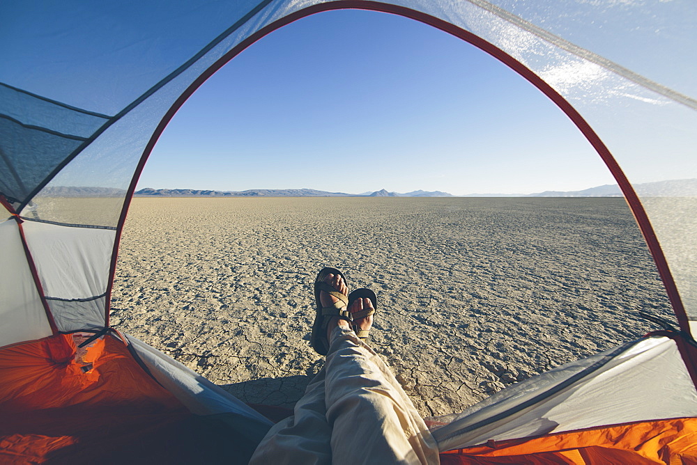 Man reclining in camping tent, expansive desert and playa in distance, Black Rock Desert, Nevada, United States of America