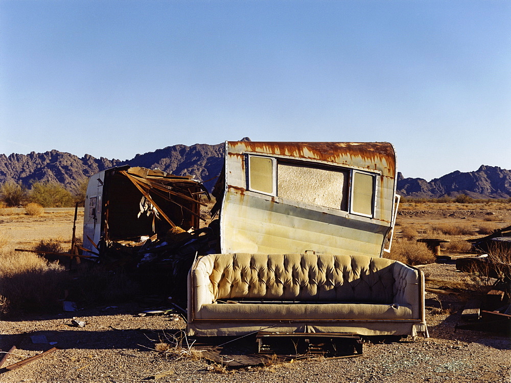 A ruined caravan, with rusting roof, a shelter, and a sofa, USA