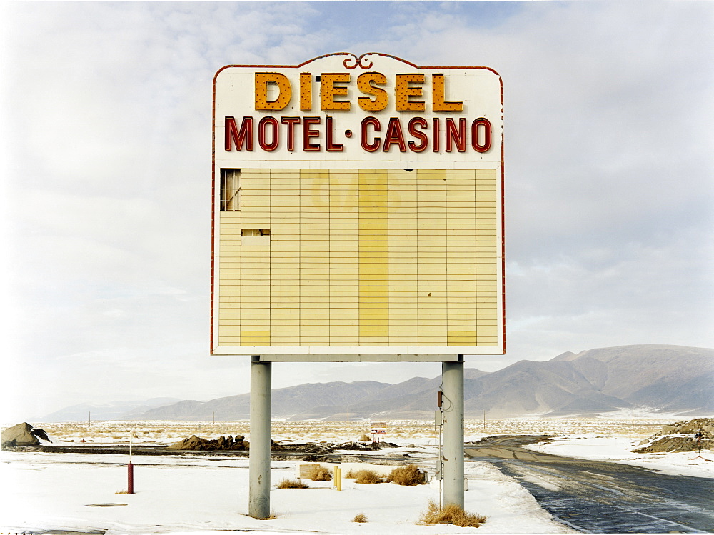 A large roadside sign in a flat landscape with light snow, Mountain range, Diesel and Motel Casino, USA