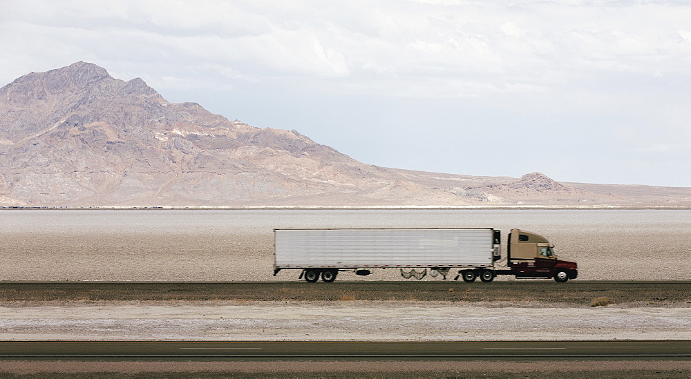 Lorry driving on a road through a desert landscape with mountains in the background.