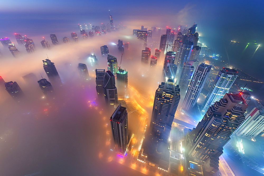 Aerial view of cityscape with illuminated skyscrapers above the clouds in Dubai, United Arab Emirates at dusk, Dubai, United Arab Emirates