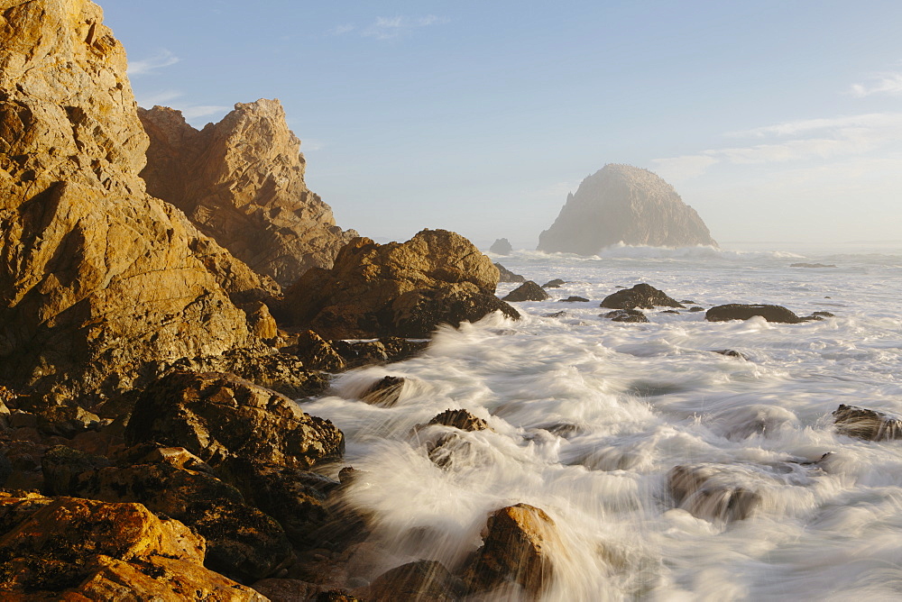 Seascape with breaking waves over rocks at dusk.