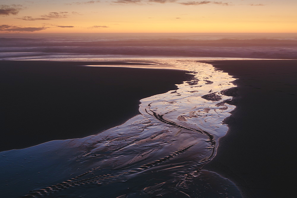 Landscape with stream flowing into ocean surf at dusk.