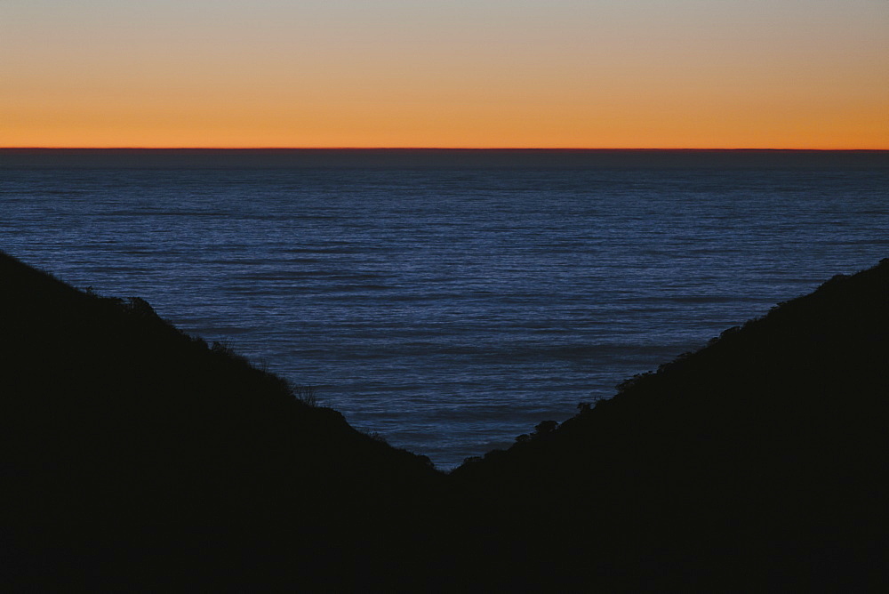 Seascape with ocean at dusk, hills in foreground.