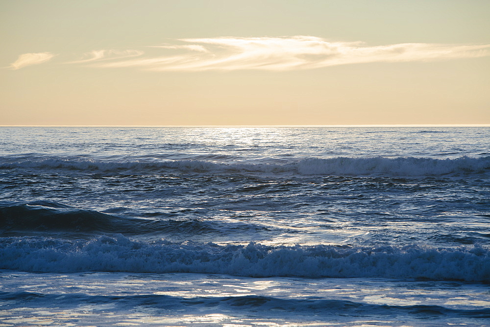 Seascape with breaking waves under cloudy sky at sunset.