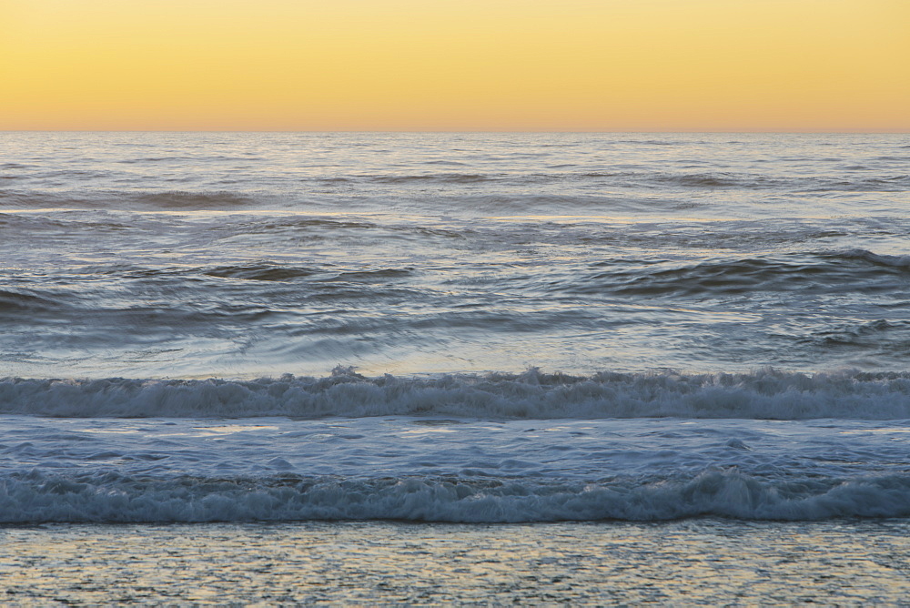 Seascape with breaking waves under cloudy sky at sunset.