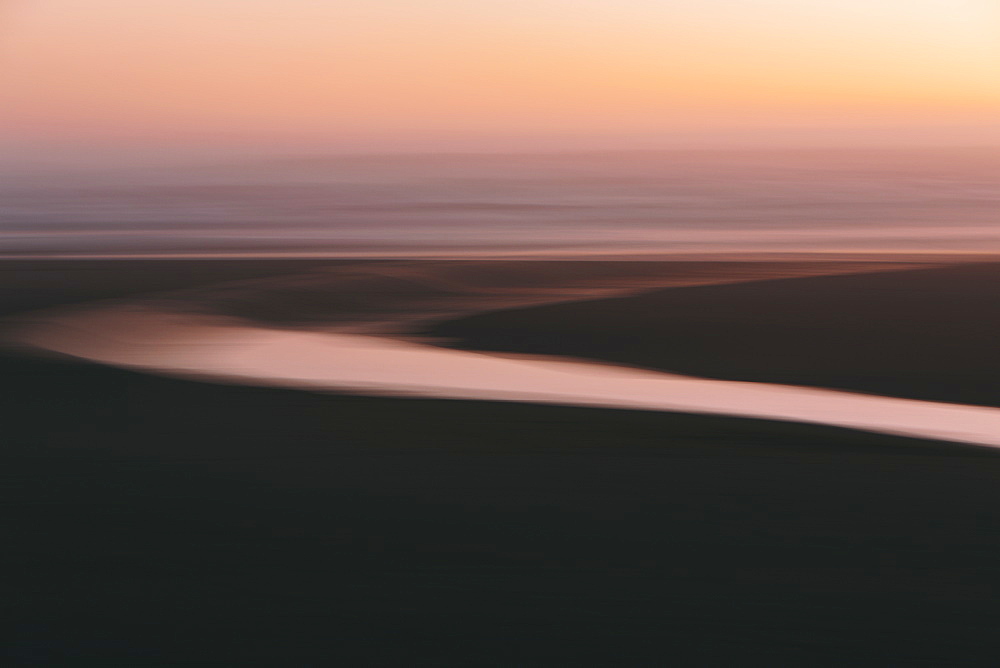 Landscape with small stream flowing into surf at dusk.