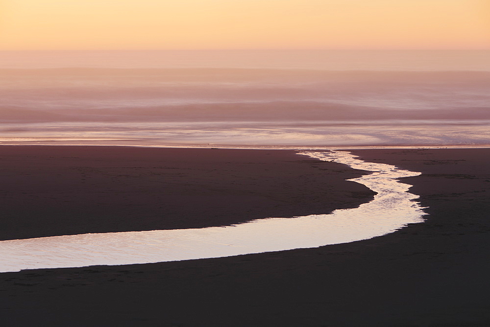 Landscape with small stream flowing into surf at dusk.