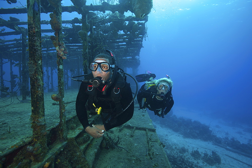 Two divers swimming along the remaining structure of a shipwreck.