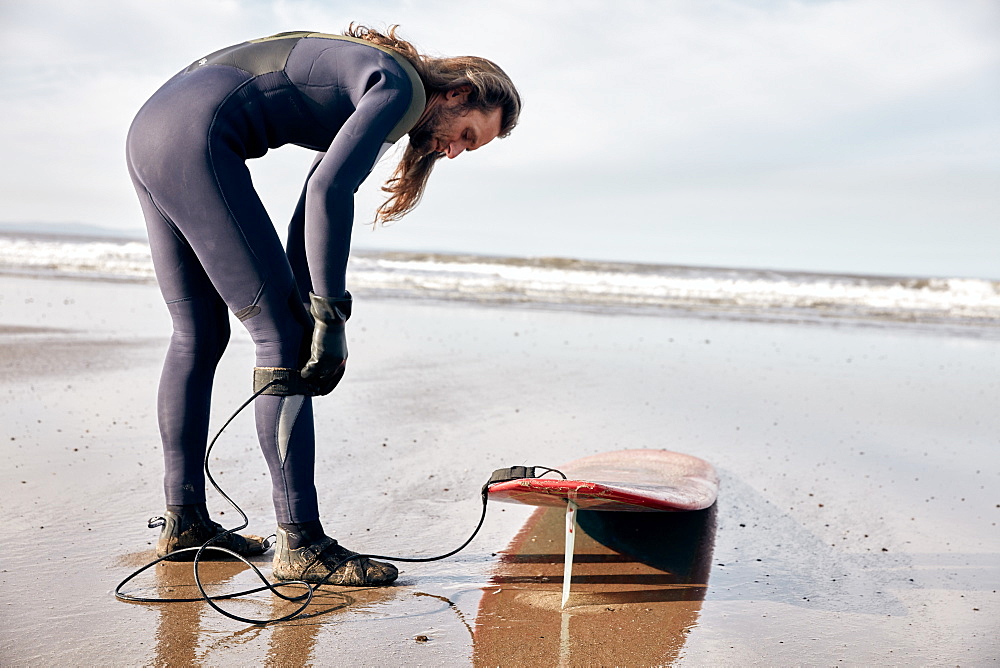 Man preparing to surf on a sandy beach in a wetsuit, United Kingdom