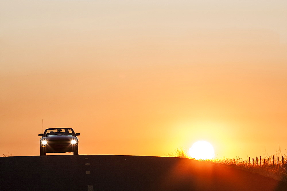 A convertible sports car on a country highway at sunset, United States of America