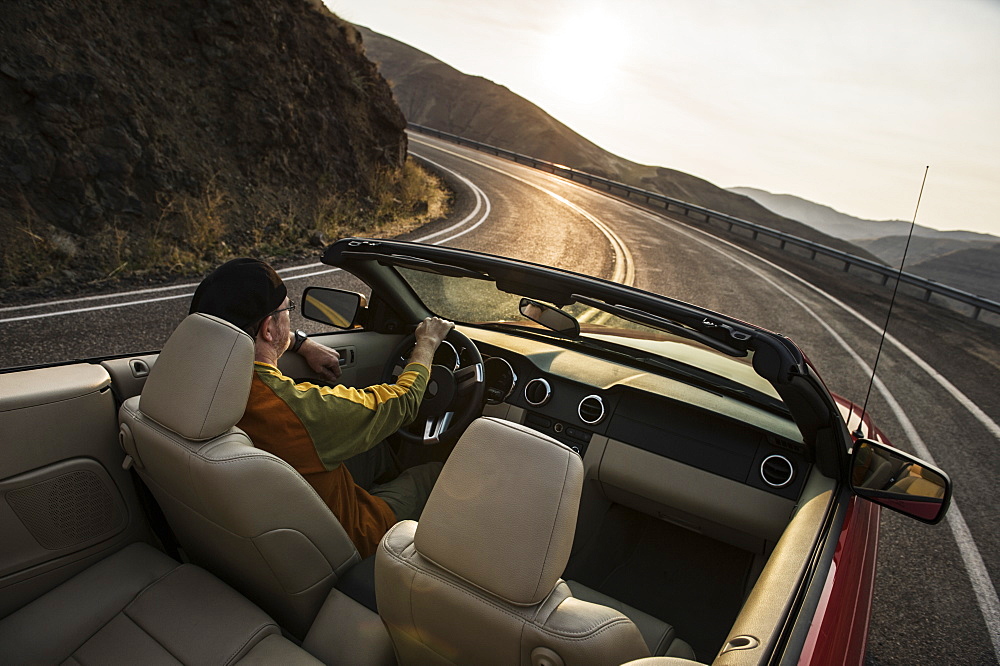 A view from behind of a Caucasian male driving a convertible sports car in eastern Washington State, United States of America