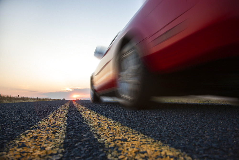 Low angle view looking up at the side of a convertible sports car on the road at sunset, United States of America