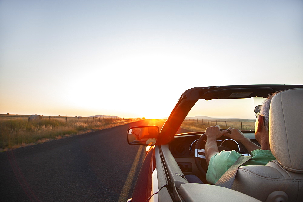 A senior Hispanic man at the wheel of his convertible sports car at sunset in eastern Washington State, United States of America