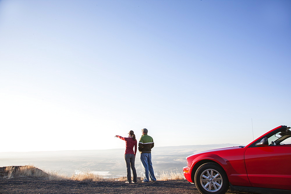 A young Caucasian couple admires the view at a rest stop in Eastern Washington, USA while on a road trip with their convertible sports car, United States of America