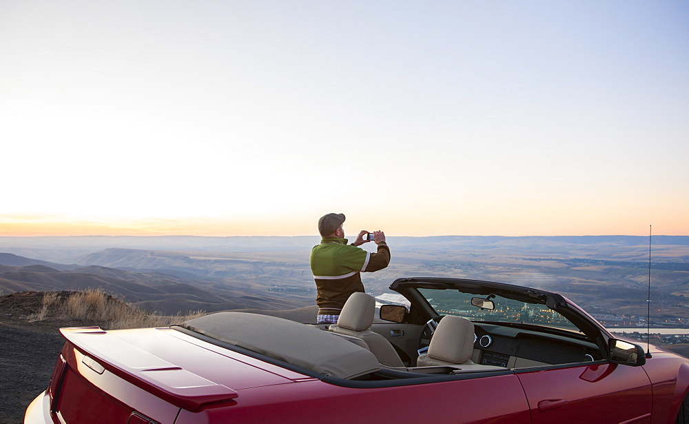 A driver stops to take a photograph at sunset near Lewiston, Idaho, USA on a road trip with his convertible sports car, United States of America