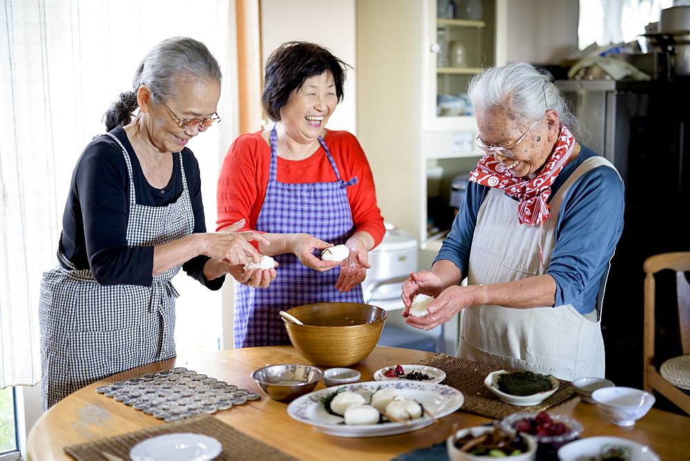 Three older women standing round a table in a kitchen, making sushi, Japan