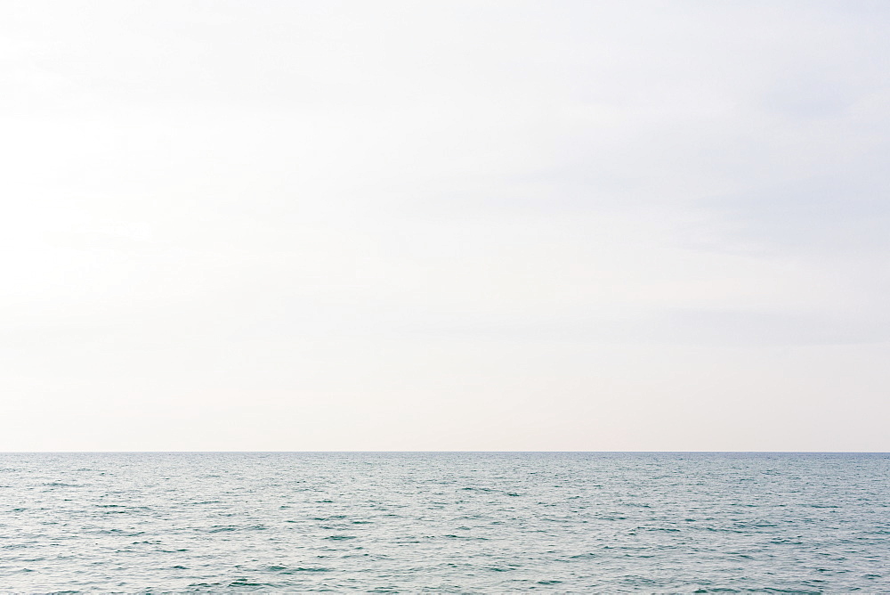 The view across a lake, a grey water surface, a view to the horizon and light cloudy sky, United States of America
