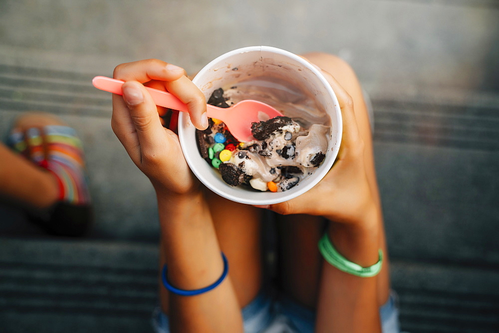 High angle close up of girl sitting on steps eating ice cream, United States of America