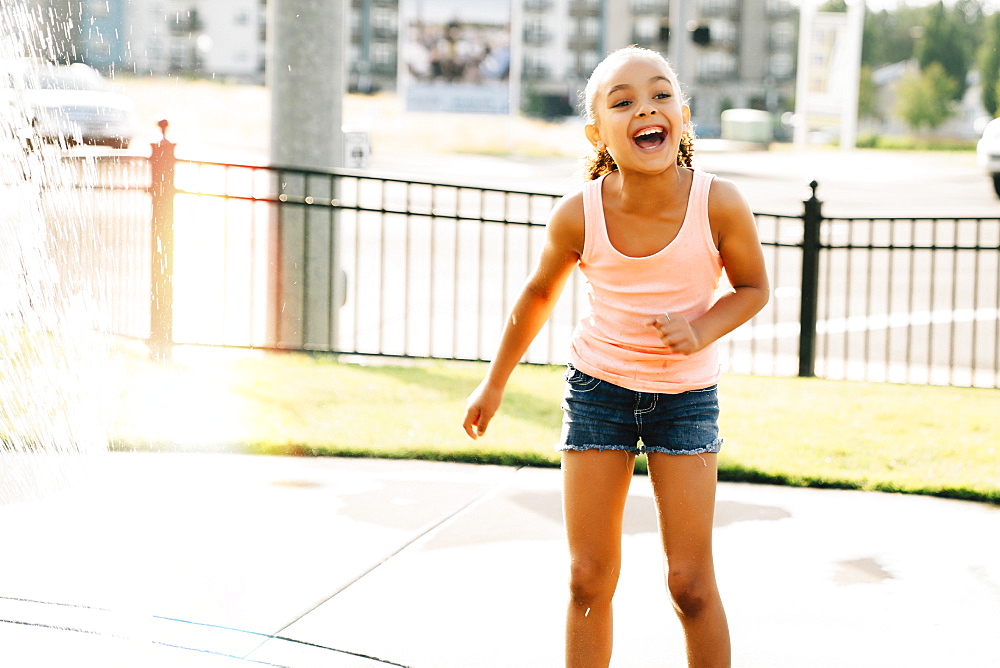 Smiling girl playing in public fountain in summer, United States of America