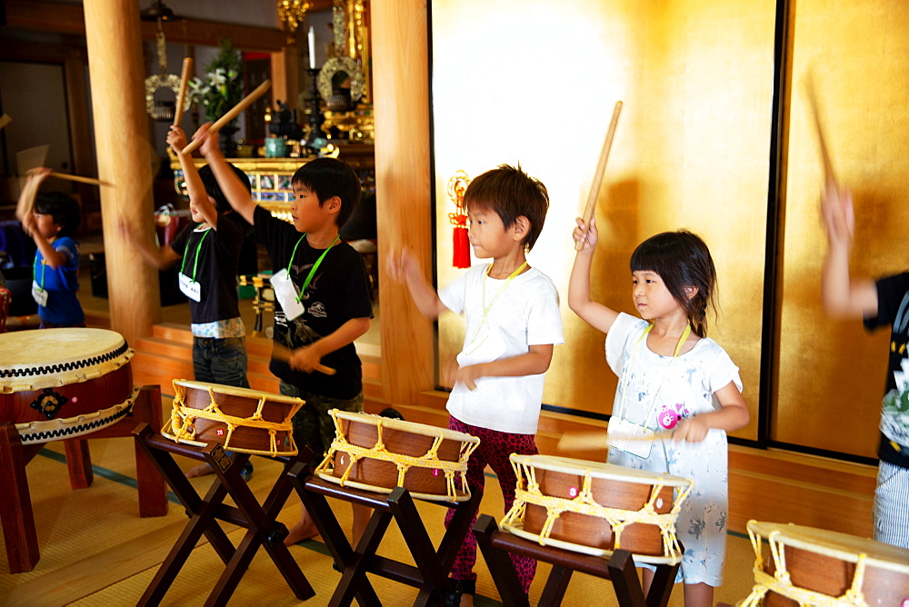 Group of pre-school children playing the drums in a Japanese temple, a traditional religious practise, Kyushu, Japan