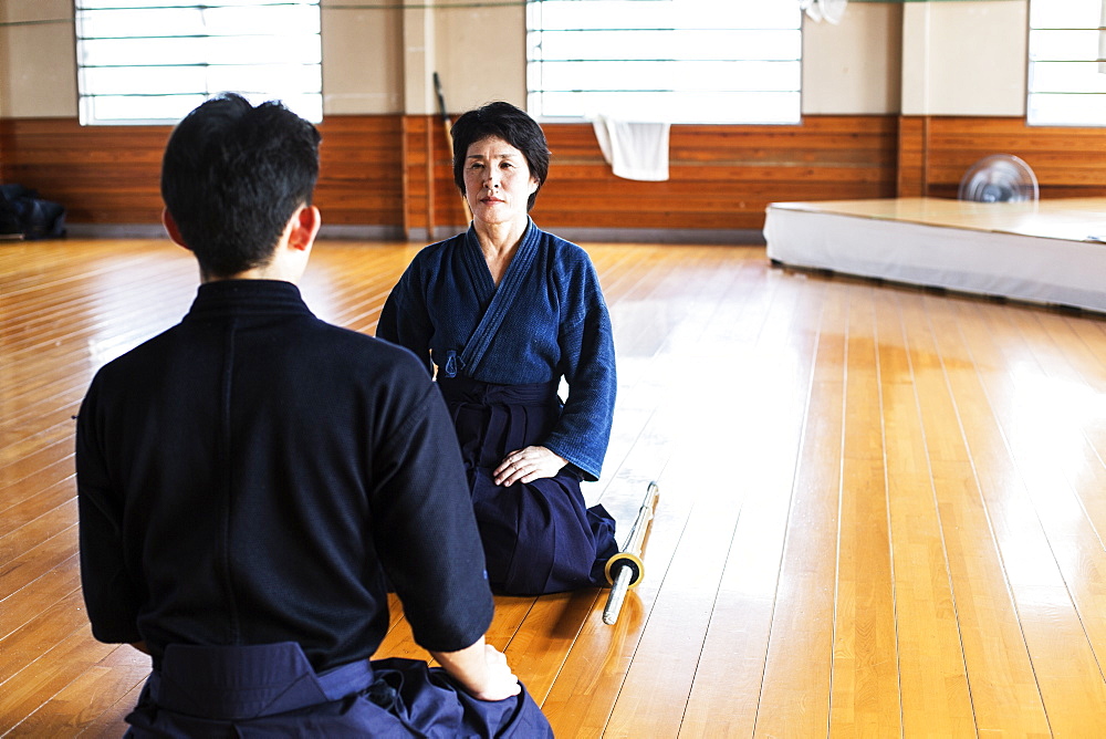 Female and male Japanese Kendo fighters kneeling opposite each other on wooden floor, Kyushu, Japan