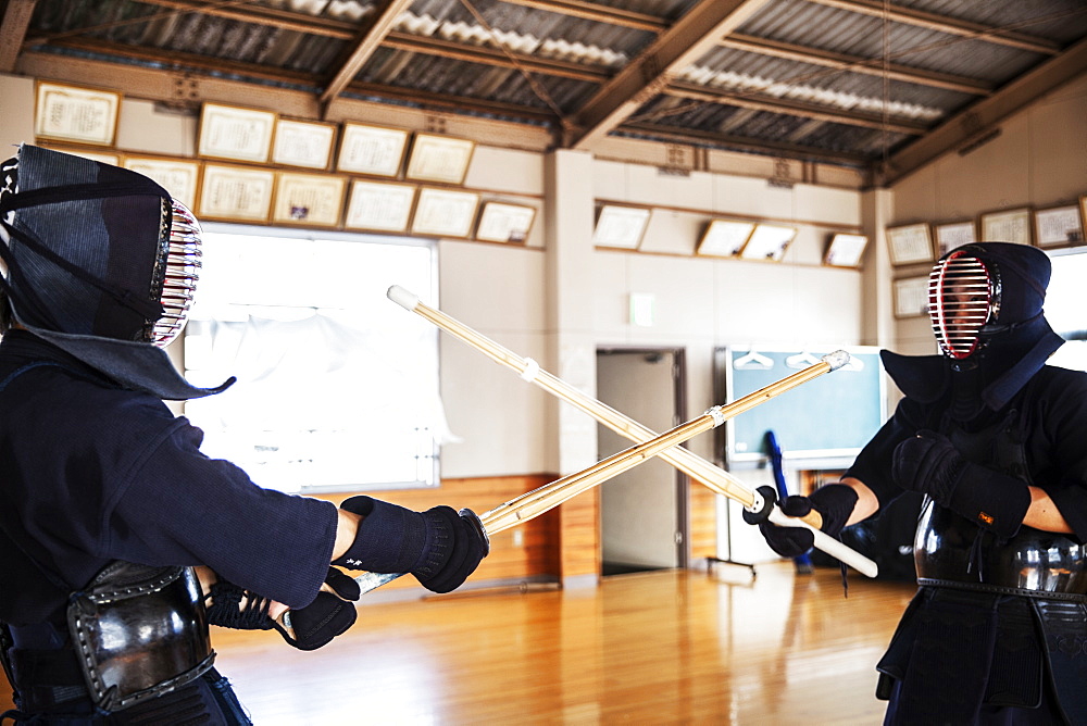 Two Japanese Kendo fighters wearing Kendo masks practicing with wood sword in gym, Kyushu, Japan