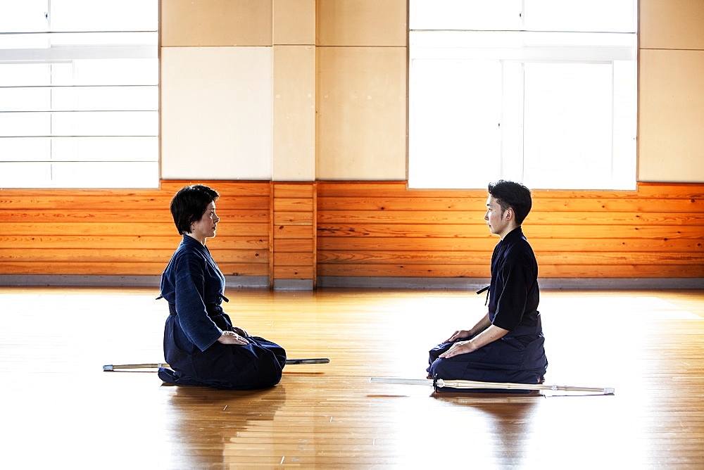 Female and male Japanese Kendo fighters kneeling opposite each other on wooden floor, Kyushu, Japan